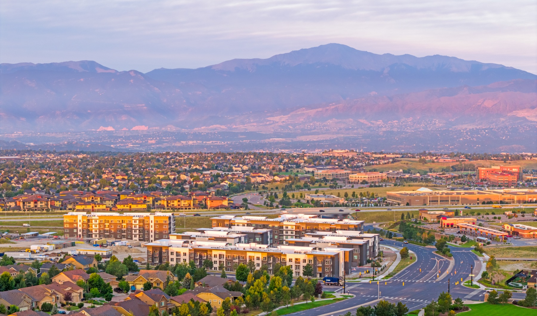 Panoramic views from your apartment Breathtaking aerial view of a vibrant cityscape with modern apartments, lush greenery, and majestic mountains under a serene sky at The Aven in Colorado Springs