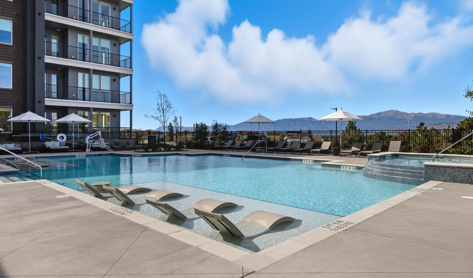 Dive in and cool off in the sparkling pool Luxurious apartment complex with a sparkling pool, stylish lounge chairs, and breathtaking mountain views under a clear blue sky at The Aven in Colorado Springs