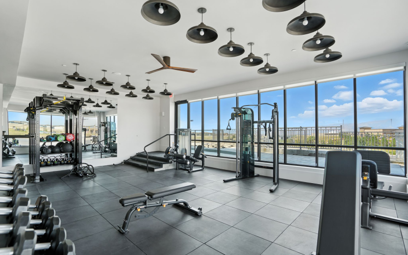 Bright and modern fitness center with state-of-the-art gym equipment, sleek black flooring, and expansive windows offering scenic views at The Aven in Colorado Springs