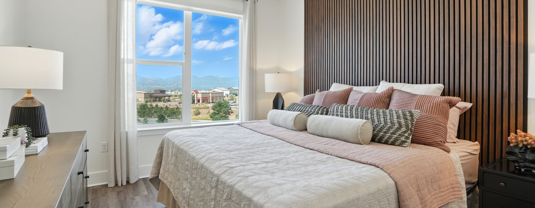 Bright bedroom with large window offering stunning mountain views, featuring elegant wood paneling, sleek ceiling fan, and plush bedding at The Aven in Colorado Springs