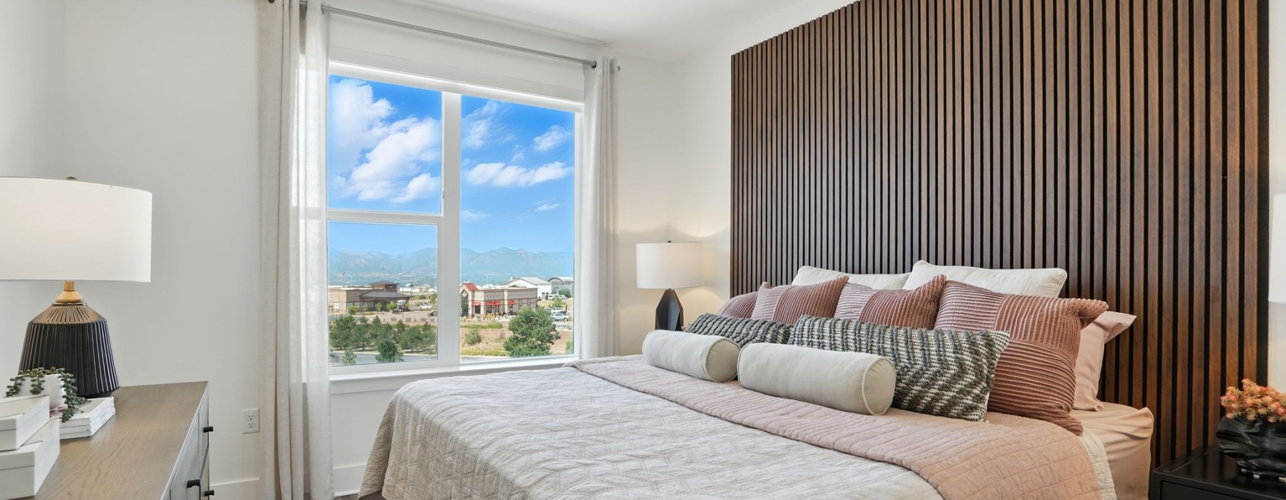 Bright bedroom with large window offering stunning mountain views, featuring elegant wood paneling, sleek ceiling fan, and plush bedding at The Aven in Colorado Springs